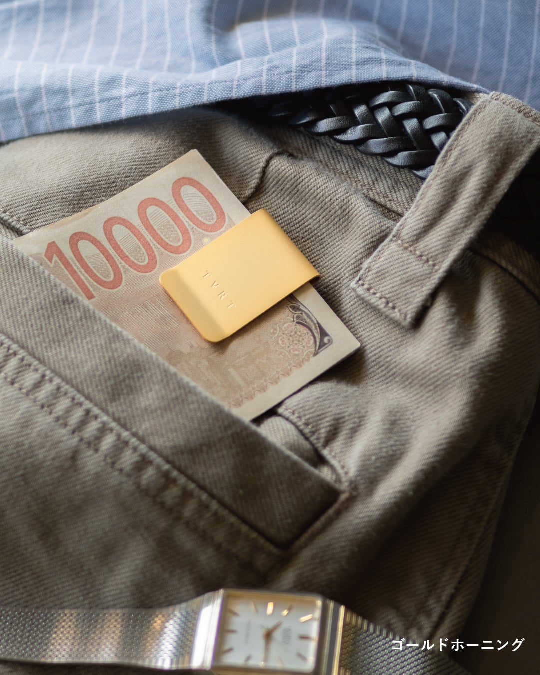 ゴールドホーニングのマネークリップで千円札を挟み、木製トレイの上で硬貨や時計と共に上品な佇まいを見せる写真。