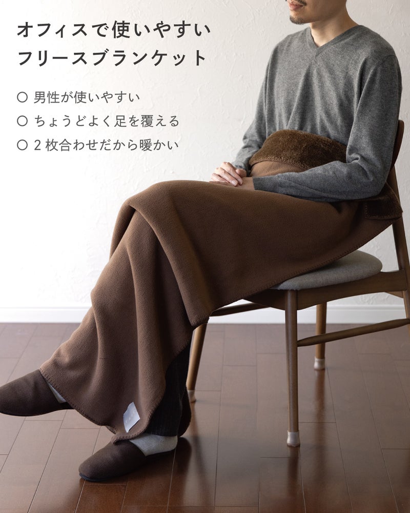 オフィスで使いやすいMr. ブランケットのブラウンをひざに掛けた男性の着用イメージで、男性向けサイズで足までちょうどよく覆える2枚合わせの暖かいフリース。