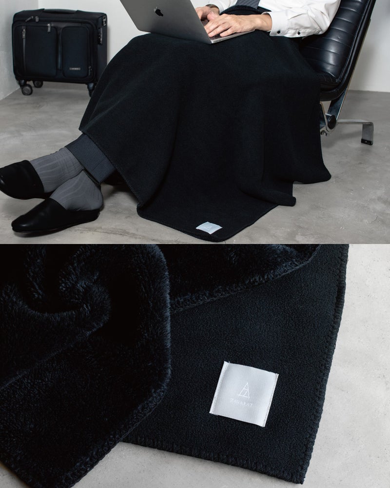 ブラックのMr. ブランケットをひざに掛けてノートパソコンで仕事をするビジネスマンと、黒い毛足の裏地とフリースが重なる生地のアップ。