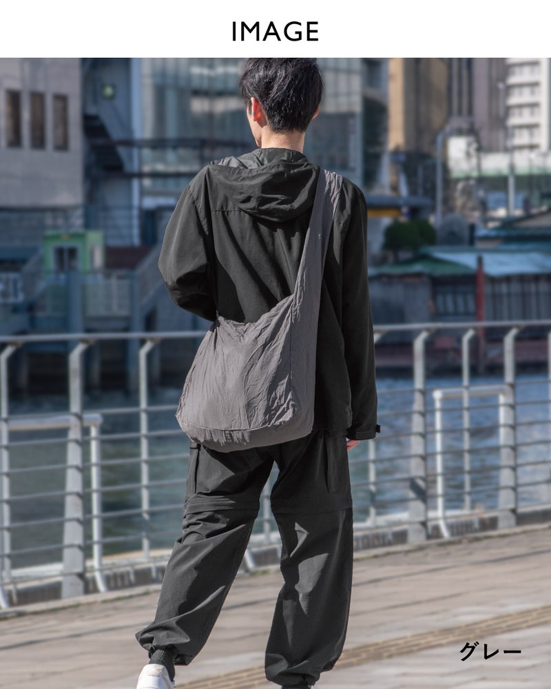 NOMAD SLING(Tav-051)グレーを斜め掛けし、水辺の遊歩道で後ろ姿を撮影した全身コーディネート画像。