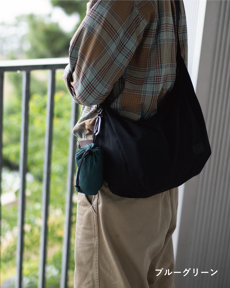 NOMAD SLING(Tav-051)ブルーグリーンにカラビナを付け、チェックシャツに合わせて斜め掛けした横向きの着用例。