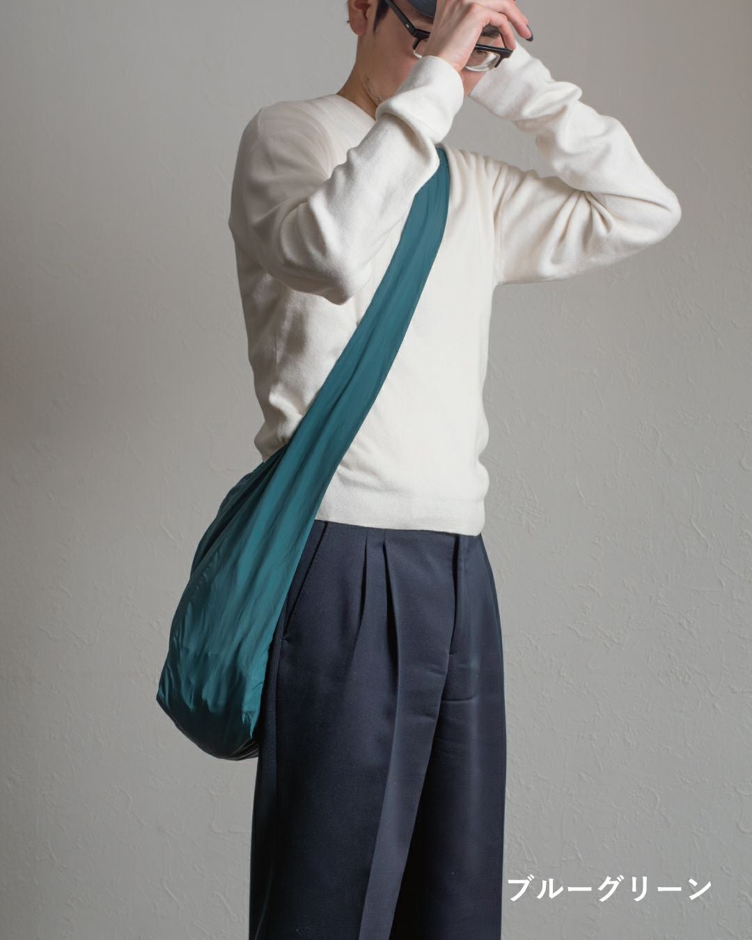 ブルーグリーンのスリングバッグと白い服の男性