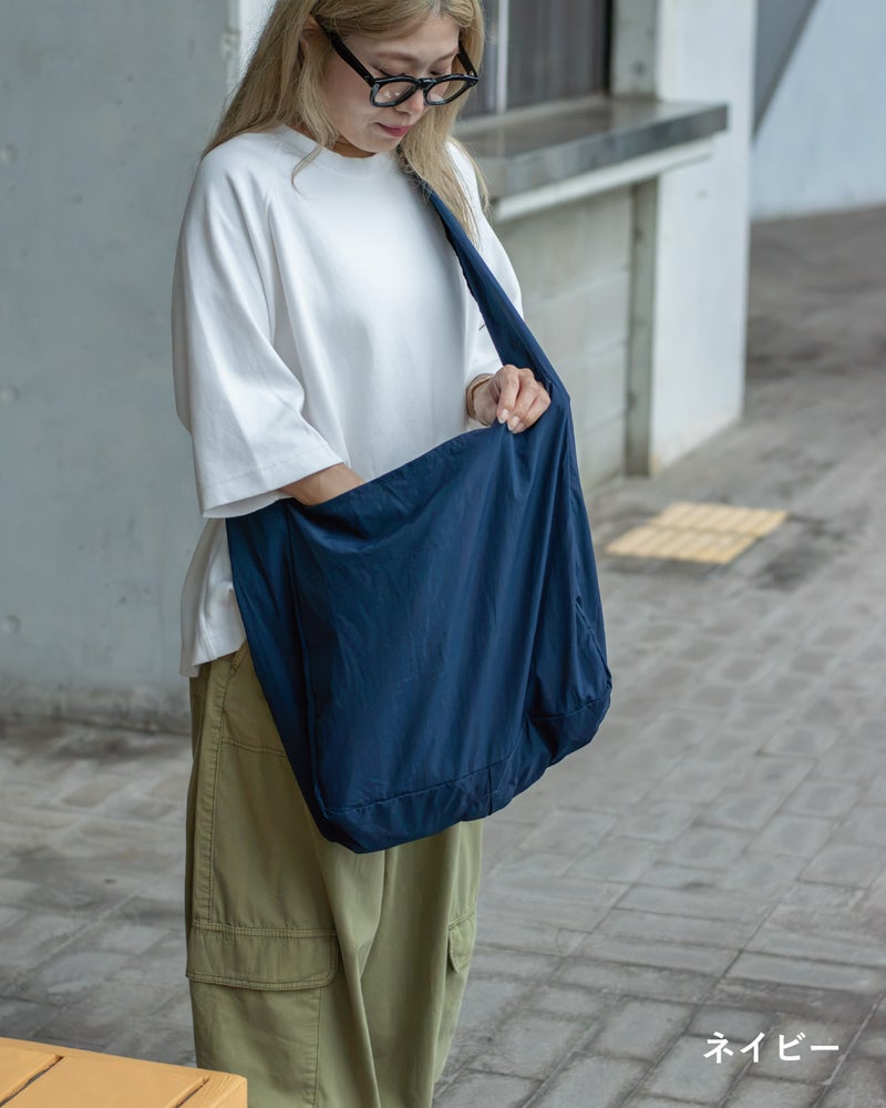 NOMAD SLING(Tav-051)ネイビーを眼鏡の女性が手に持ち、丸みのあるシルエットを正面から見せた画像。