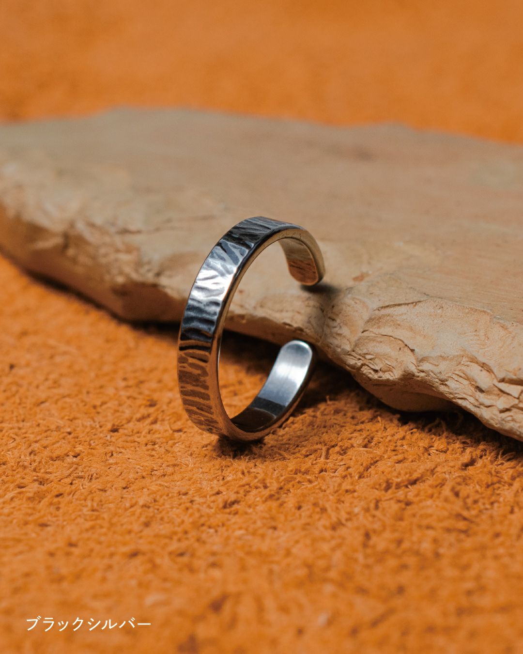 オレンジのファブリック上に置かれた石と、その上に立てかけられた槌目模様のブラックシルバーリング