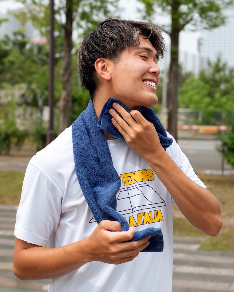 屋外ランニング後にブルーのマフラータオルで笑顔で汗を拭く男性。今治タオル認定の高吸水性がアウトドアスポーツの発汗をしっかり吸い取る。
