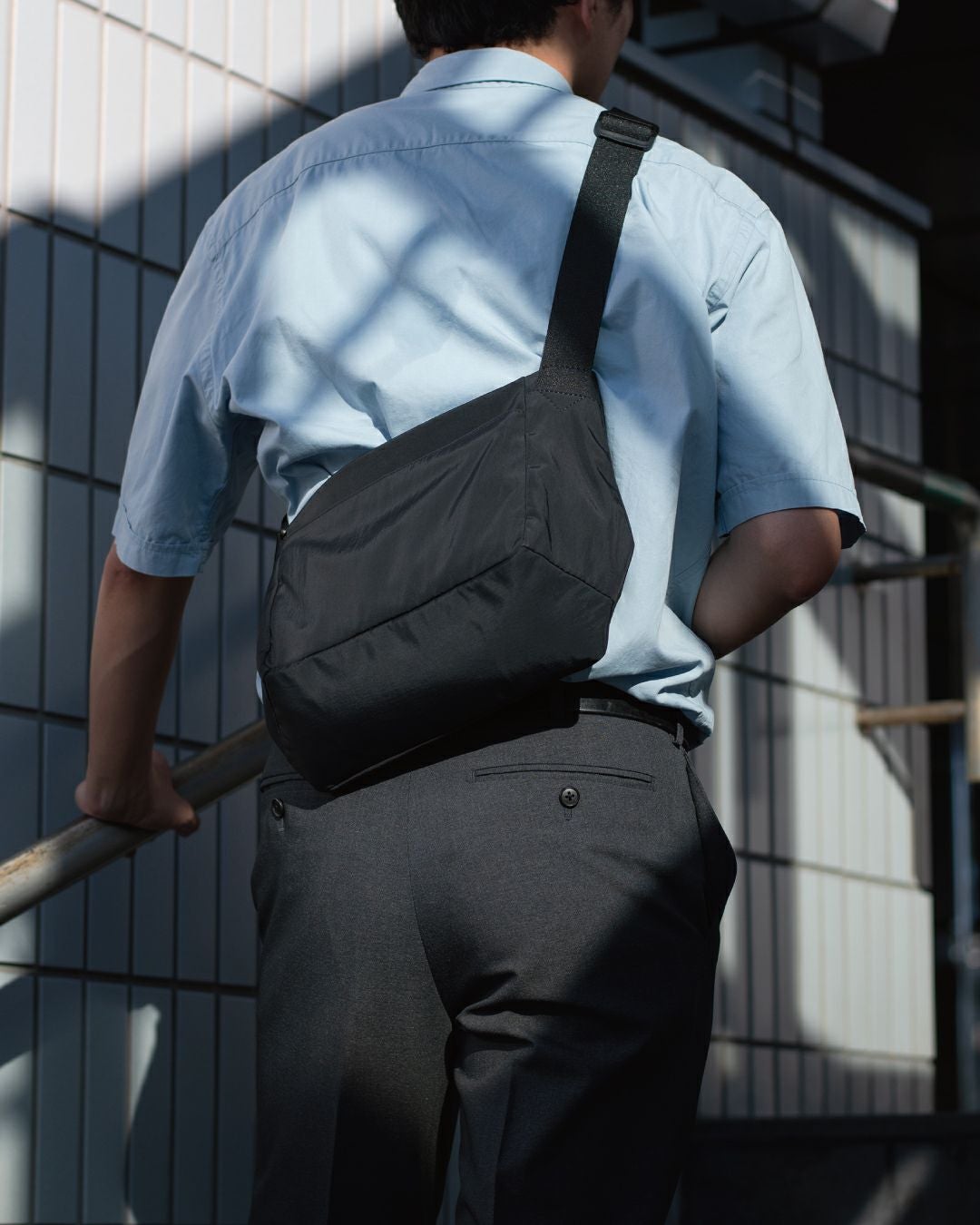 男性がブラックのメンズショルダーバッグを斜めがけにしている全身ショット。シンプルなデザインが特徴。