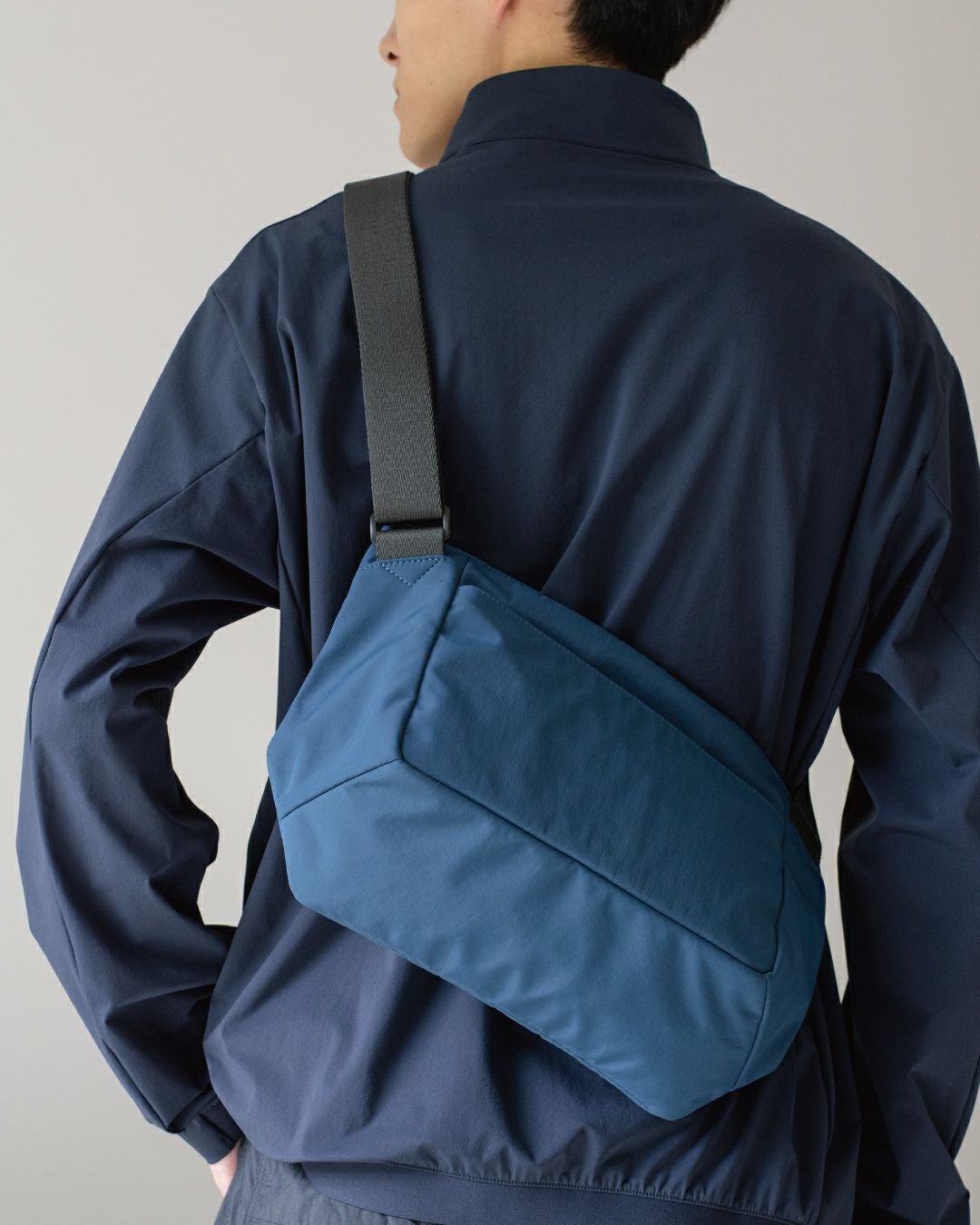 男性がネイビーのメンズショルダーバッグを背中に背負っている姿。バッグの背面からの見た目。
