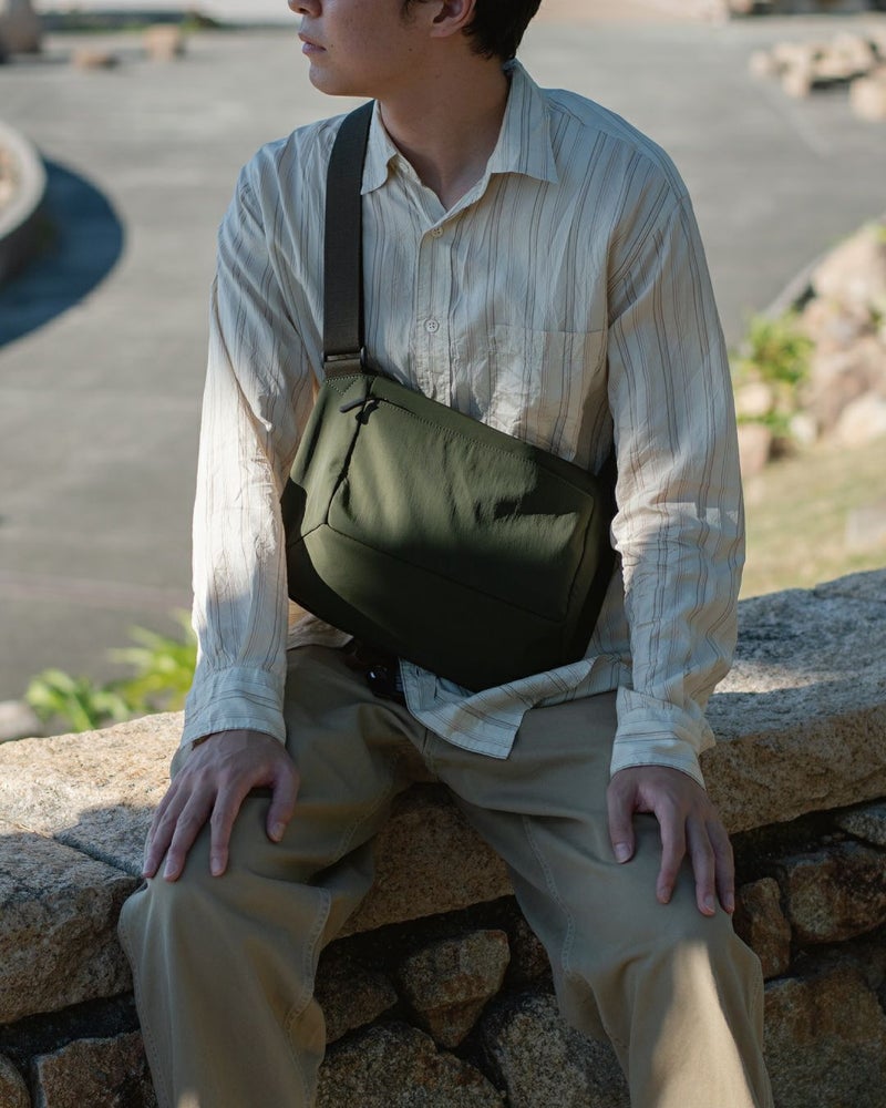 男性がカーキ色のメンズショルダーバッグを斜めがけにしているクローズアップ。