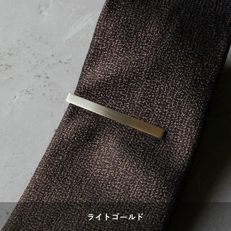 黒地に茶色の柄のネクタイに着用されたライトゴールドのシンプルなネクタイピン。