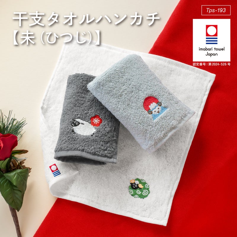 灰色と薄灰色の2枚を重ね、紅白の布や松、ばらとともに飾った今治産干支タオルハンカチ未(ひつじ)の新年ギフトイメージ。