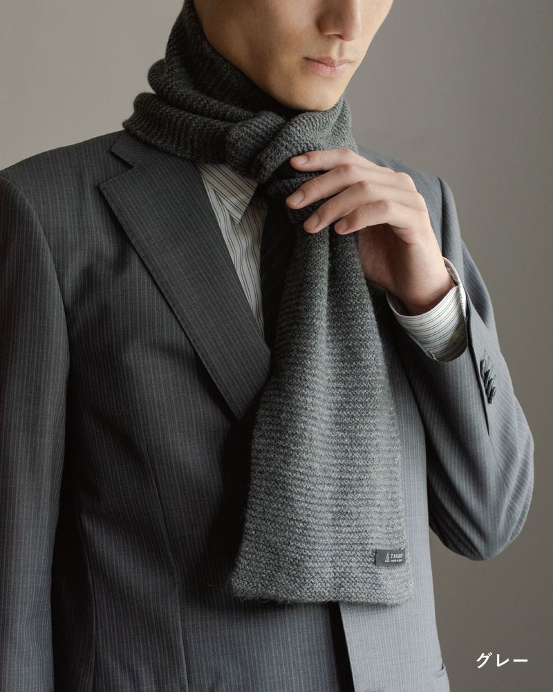 グレー色のタック編み 3秒マフラーを巻いた男性の着こなし。ビジネススーツに合わせやすい色と編み地。