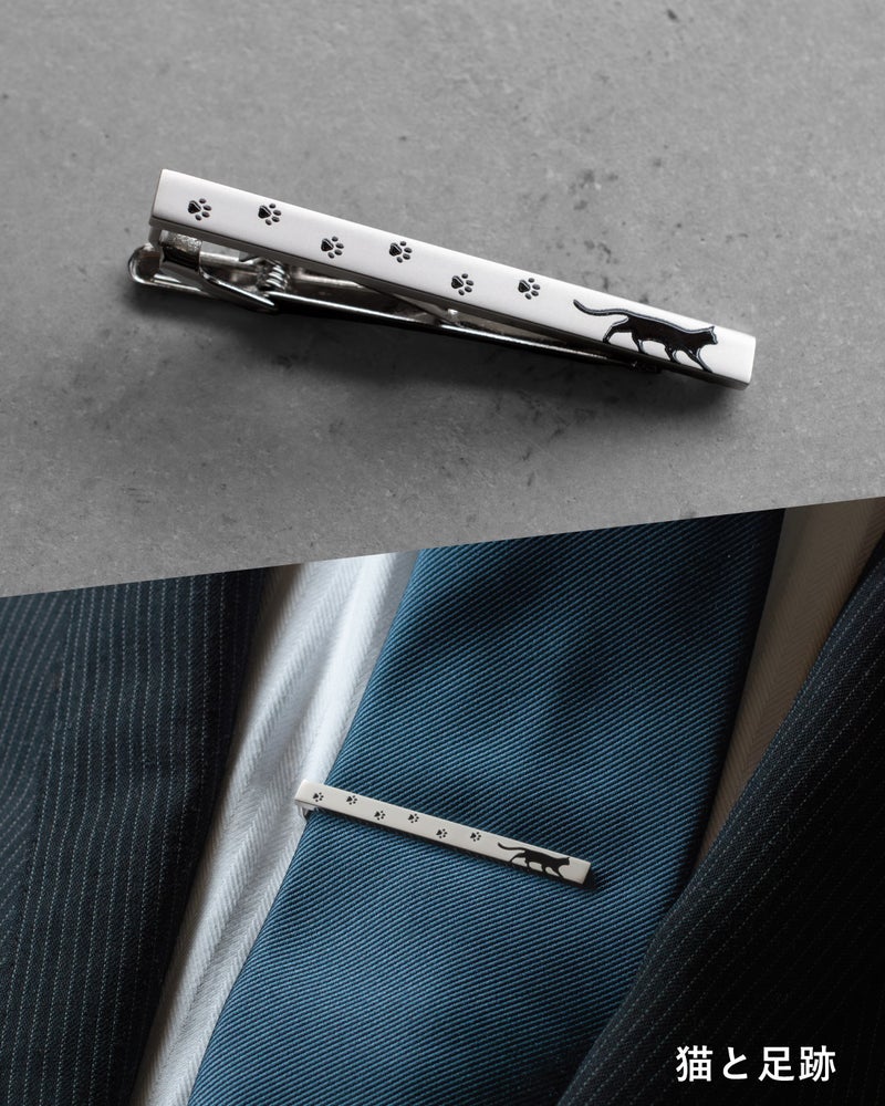 「猫と足跡」モデルの詳細。白いベースに黒い猫のシルエットと点々と続く足跡がデザインされたネクタイピン単体と、スーツへの着用カット。