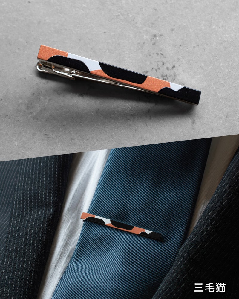 「三毛猫」モデル。白・黒・オレンジの三毛猫模様を大胆にプリントしたネクタイピン。遊び心のあるデザインが、ビジネススーツの胸元にさりげない個性を加えている。