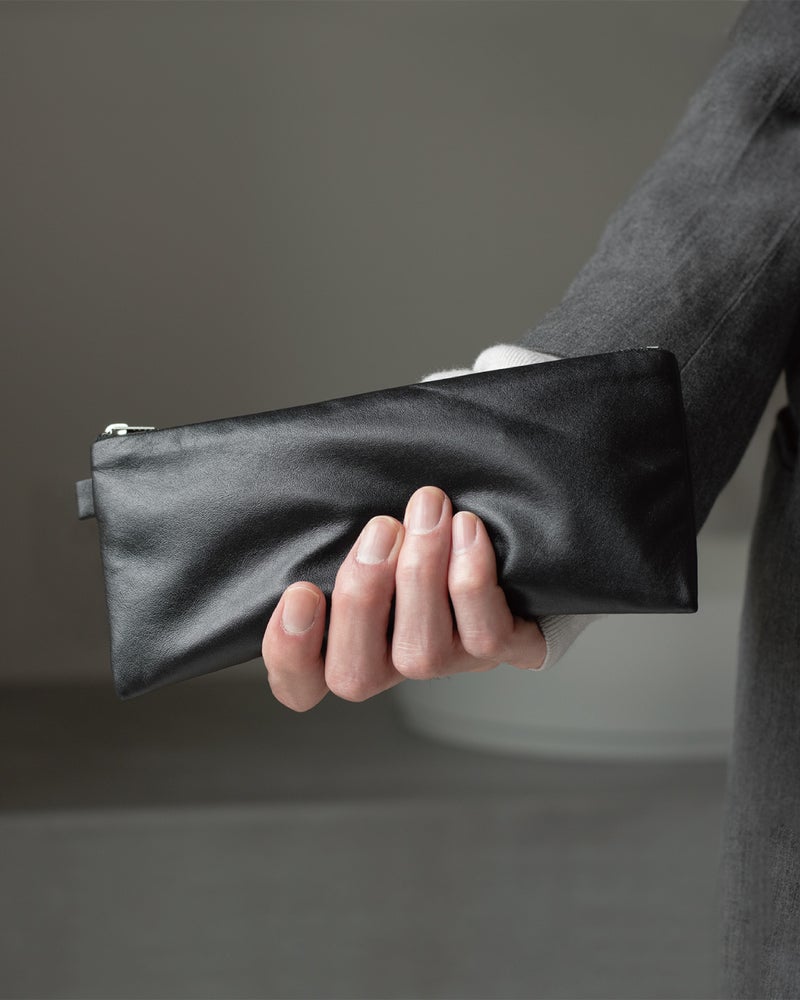 片手でFOLMAブラックナッパーレザーポーチPENを握り持つクローズアップ。200mmの細長フォルムが手にしっとりなじむ軽量本革ペンケースの持ちやすさを伝えるビジュアル。
