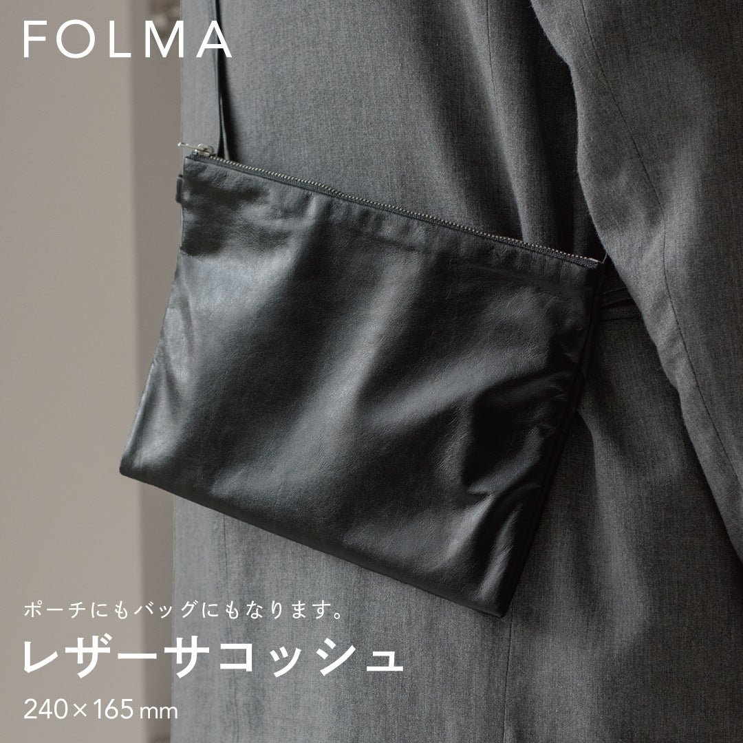 FOLMAレザーサコッシュ（240×165mm）をスーツの脇に斜めがけしたスタイリング。ポーチにもバッグにもなる2WAY仕様のブラックナッパーレザー製サコッシュ。