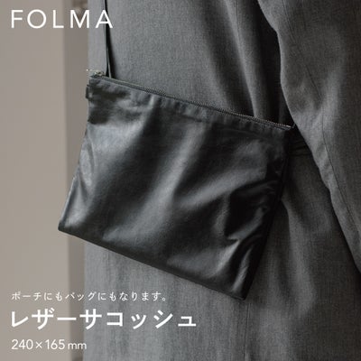 FOLMAレザーサコッシュ（240×165mm）をスーツの脇に斜めがけしたスタイリング。ポーチにもバッグにもなる2WAY仕様のブラックナッパーレザー製サコッシュ。