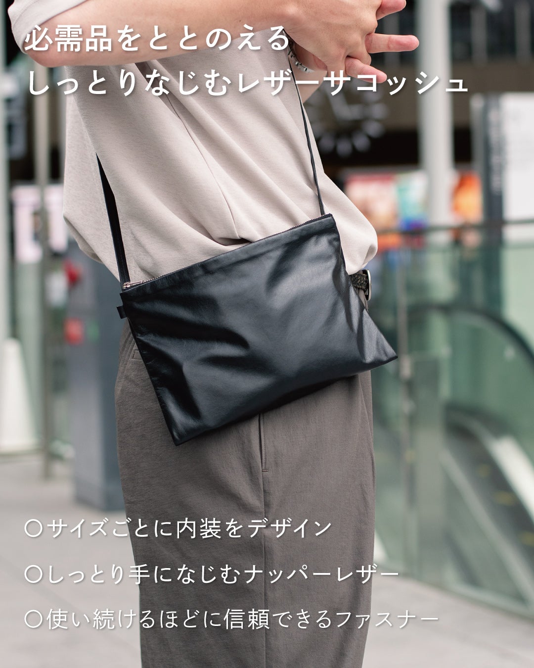 スーツ姿でFOLMAレザーサコッシュをショルダーストラップで斜めがけして手を添えるビジネスコーデ。ナッパーレザーとYKKファスナー採用で毎日の必需品をしっとりなじむ本革でまとめる。