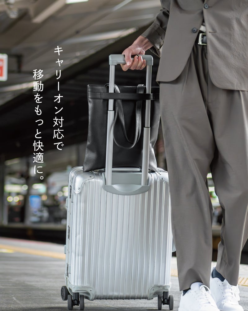 駅のホームでキャリーケースのハンドルにFOLMAビジネストートを通して固定する様子で、出張や旅行時の移動もスムーズになる対応力を紹介。
