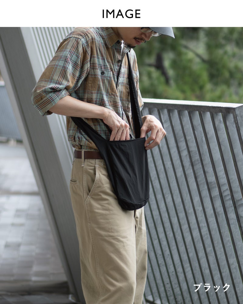 NOMAD SLING(Tav-051)のブラックを斜め掛けにし、バッグの中に手を入れて荷物を取り出す着用シーン。