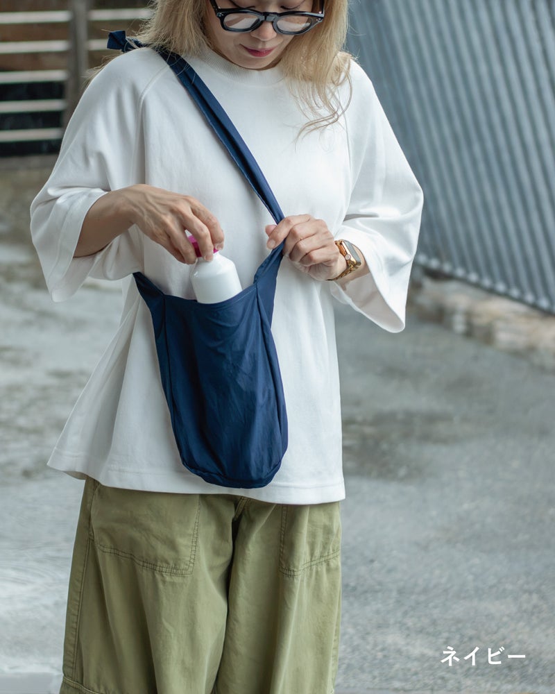 NOMAD SLING(Tav-051)のネイビーにスプレーボトルを入れる様子を写した、開口部の使いやすさが分かるカット。