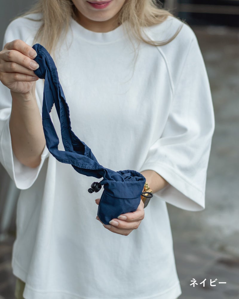 NOMAD SLING(Tav-051)のネイビーを手に持ち、収納ポーチからストラップを伸ばして広げる瞬間を捉えたカット。
